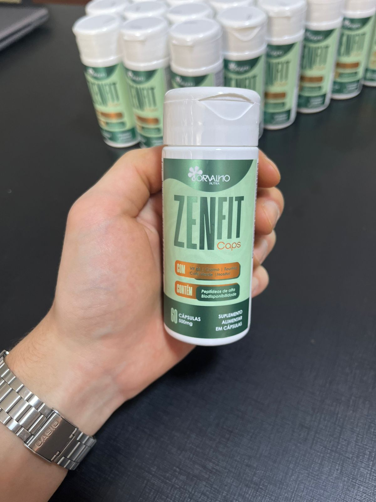 Frasco do ZenFIT Caps segurado na mão com estoque ao fundo